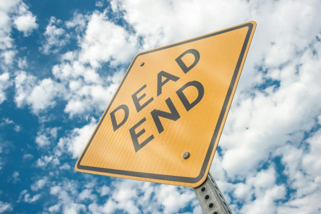 a dead end road sign against a bright, cloudy blue sky, symbolizing restriction and caution.