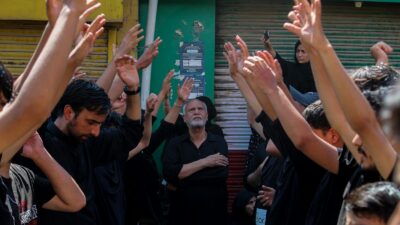 Participants in an Ashura procession in Srinagar raise their hands in a religious gathering outdoors.