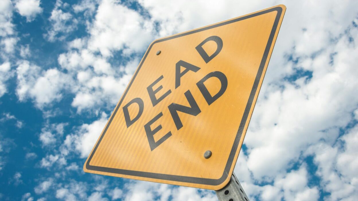 Close-up of a dead end road sign against a bright, cloudy blue sky, symbolizing restriction and caution.