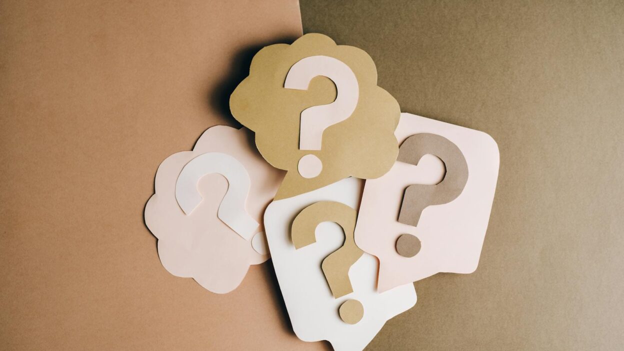 Question mark cutouts in layered paper craft style on a brown backdrop, conceptual art.