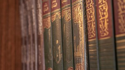 Books with arabic writing are on a wooden shelf.