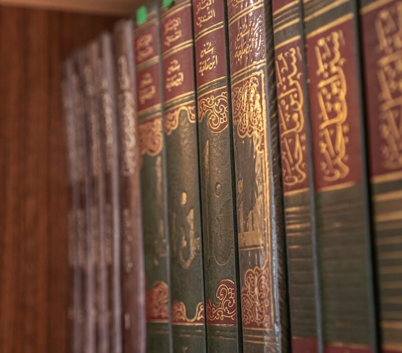 Books with arabic writing are on a wooden shelf.